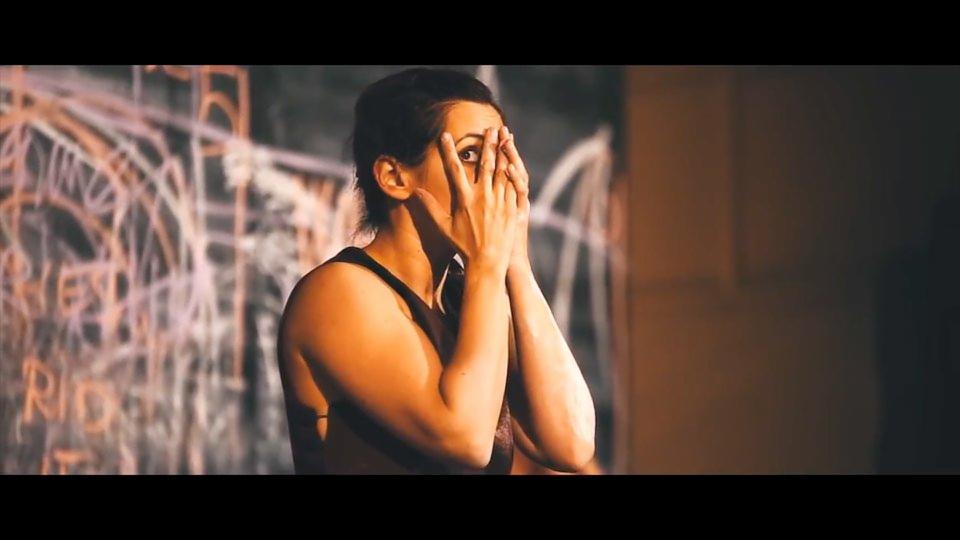 Kobieta zakrywa twarz dłońmi, spoglądając przez palce na tle ściany z graffiti podczas kręcenia sceny.