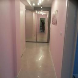 NEST BUDOWNICTWO Karol Flis - Korytarz po odświeżeniu, ściany pomalowane na jasny róż, błyszcząca podłoga z płytek, w głębi lustrzane drzwi przesuwne szafy wnękowej, odbijające sylwetkę osoby.