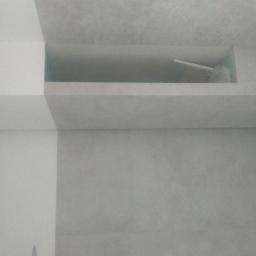 NEST BUDOWNICTWO Karol Flis - Minimalistyczna łazienka z szarą, teksturowaną ścianą, wbudowaną półką w ścianie nad umywalką i owalną, podwieszaną umywalką z chromowaną baterią.