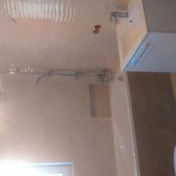 NEST BUDOWNICTWO Karol Flis - Wykończona łazienka z beżowymi płytkami, białą umywalką z szafką, toaletą i prysznicem z deszczownicą, widok z dołu pod kątem.