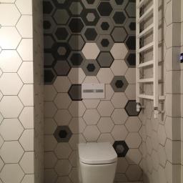 NEST BUDOWNICTWO Karol Flis - Nowoczesna łazienka z heksagonalnymi płytkami w odcieniach szarości i bieli, podwieszana toaleta i biały grzejnik drabinkowy.