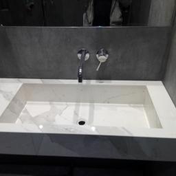 NEST BUDOWNICTWO Karol Flis - Nowoczesna łazienka z umywalką z białego marmuru, chromowaną armaturą i szarą, betonową ścianą w tle, z czarnym gniazdkiem elektrycznym po prawej stronie.