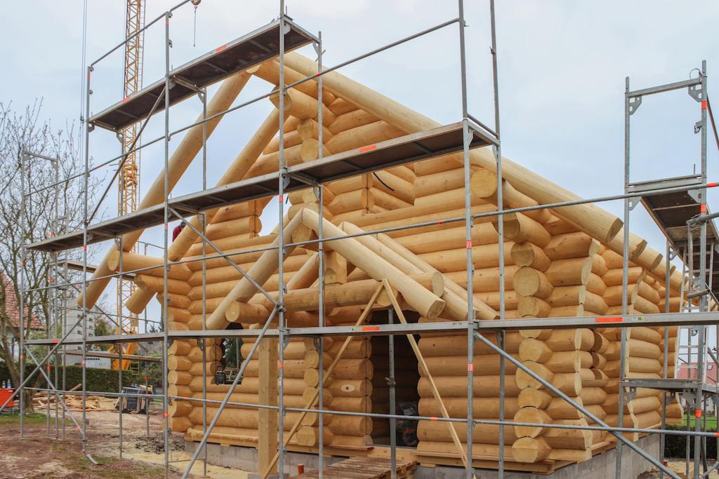 Surowy stan budowy domu z okrąglaków, widoczne rusztowania i elementy konstrukcyjne dachu.