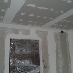 Etna - Ściany i sufit w trakcie szpachlowania, zabezpieczone folią drzwi w tle, widoczne puszki elektryczne.