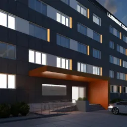 Wizualizacja budynku biurowego z ciemną elewacją, pomarańczowym wejściem i napisem 'Lubińskie Centrum Biznesu' na górze, widok z zewnątrz na parking i zieleń.