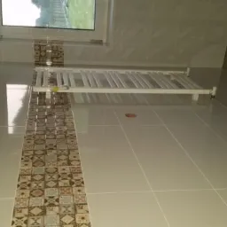 Wykończona łazienka z beżowymi płytkami, dekoracyjnym pasem z wzorzystych płytek oraz białym grzejnikiem drabinkowym pod oknem.