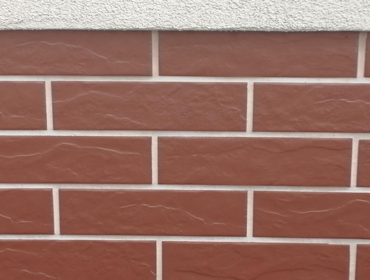 Fragment ściany z brązowych cegieł klinkierowych i białej fugi, z widoczną fakturą tynku na górze.