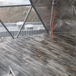 Wnętrze kopuły geodezyjnej w Zakopanem z drewnopodobnymi płytkami na podłodze, widoczna maszyna do cięcia płytek i izolacja ścian.