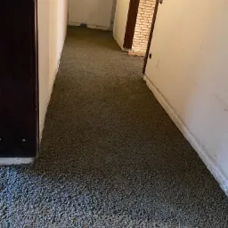 Świeżo wylana, szara, wilgotna masa na podłodze korytarza, widoczne ściany i drzwi w tle.