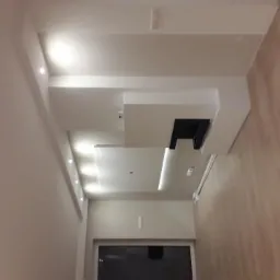 Nowoczesny sufit podwieszany z oświetleniem punktowym i liniowym, drewniana podłoga, kremowe ściany.