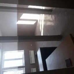 Wnętrze korytarza po remoncie, z widocznymi grzejnikami, oknami i pomalowanymi ścianami na dwa kolory, z szarymi filarami konstrukcyjnymi.