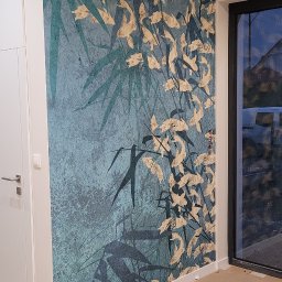 Glazurnictwo-Remonty - Ściana z tapetą w odcieniach turkusu i złota z motywem bambusa i liści, widok na fragment podłogi zabezpieczonej kartonem podczas prac wykończeniowych.