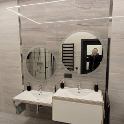 Glazurnictwo-Remonty - Nowoczesna łazienka z dwoma okrągłymi lustrami z podświetleniem LED, umywalkami nablatowymi i płytkami imitującymi naturalny kamień, z widocznym odbiciem osoby robiącej zdjęcie.
