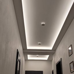 Glazurnictwo-Remonty - Nowoczesny korytarz z podwieszanym sufitem z oświetleniem LED, punktowe lampy sufitowe, ciemne drzwi z przeszkleniami i subtelne oświetlenie podłogowe.