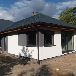 Nowoczesny dom jednorodzinny z szarą blachodachówką, białymi ścianami z szarymi akcentami i dużymi oknami, widok z zewnątrz na częściowo zagospodarowany teren.