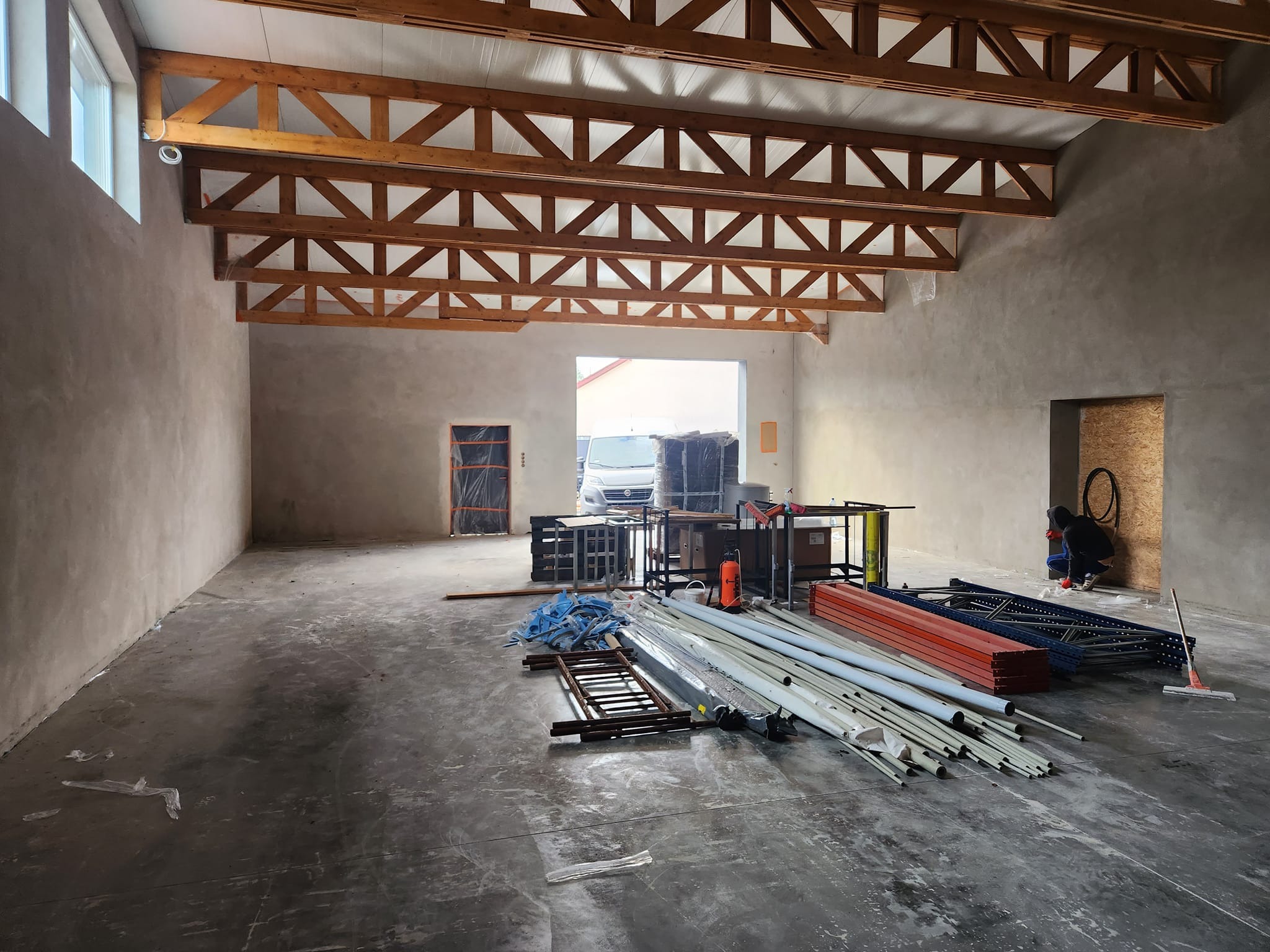 Wnętrze hali po nałożeniu szarego tynku maszynowego, widoczne drewniane elementy konstrukcji dachu, przygotowane rusztowania i narzędzia do dalszych prac.