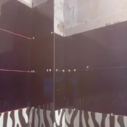 Układanie ciemnych płytek w łazience z dolnym rzędem płytek w zebrę, widoczny laserowy niwelator i krzyżyki dystansowe, surowy stan ściany nad płytkami.