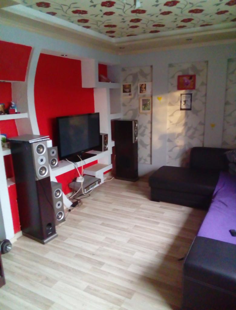 Pokój dzienny po odświeżeniu, z czerwono-białą ścianą TV, gładzią na ścianach, wzorzystym sufitem i jasną podłogą imitującą drewno.