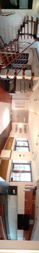 Wnętrze domu z drewnianymi schodami z metalowymi balustradami, parkietem, oknami z drewnianymi ramami, białymi ścianami i sufitem z oświetleniem punktowym.