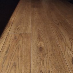 MB Constructions Michał Borkowski - Ułożone panele podłogowe z wyraźnym wzorem drewna, sfotografowane pod kątem z bliska, z delikatnym oświetleniem podkreślającym fakturę.