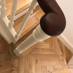 MB Constructions Michał Borkowski - Parkiet ułożony we wzór jodełki francuskiej, białe schody z ciemnobrązową poręczą, widok z góry.