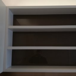 MB Constructions Michał Borkowski - Wnęka z trzema półkami w kolorze białym, z brązowym tłem, widoczne odbicie fotografa.