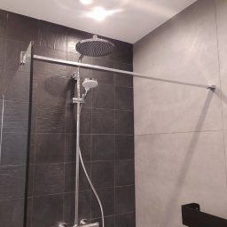 MB Constructions Michał Borkowski - Nowoczesna kabina prysznicowa z deszczownicą i baterią termostatyczną, wykończona czarnymi płytkami imitującymi kamień i szarymi płytami wielkoformatowymi.