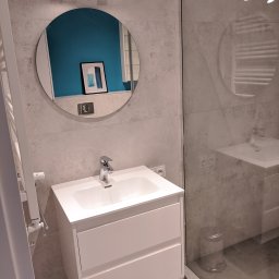 MB Constructions Michał Borkowski - Nowoczesna łazienka z umywalką nablatową na białej szafce z szufladami, okrągłe lustro z oświetleniem punktowym i kabina prysznicowa ze szklaną ścianką.