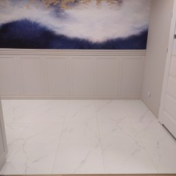 MB Constructions Michał Borkowski - Wykończone wnętrze z białymi płytkami imitującymi marmur, panelami ściennymi w kolorze kremowym i tapetą z motywem górskim w odcieniach granatu i złota.