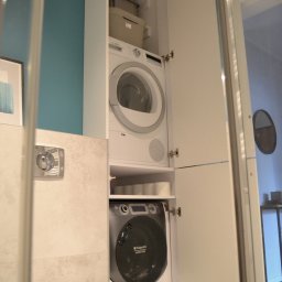 MB Constructions Michał Borkowski - Kompaktowa zabudowa w łazience: pralka i suszarka w szafie, nad toaletą, z turkusową ścianą w tle.