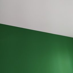 MB Constructions Michał Borkowski - Ściana pomalowana na intensywny zielony kolor, kontrastująca z białym sufitem, widoczna z perspektywy dolnej, ukazująca gładką powierzchnię i subtelne przejścia tonalne.