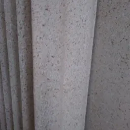 Beżowa powierzchnia ściany z drobnymi brązowymi plamkami, wykonana techniką natryskową, widoczne delikatne nierówności i faktura.