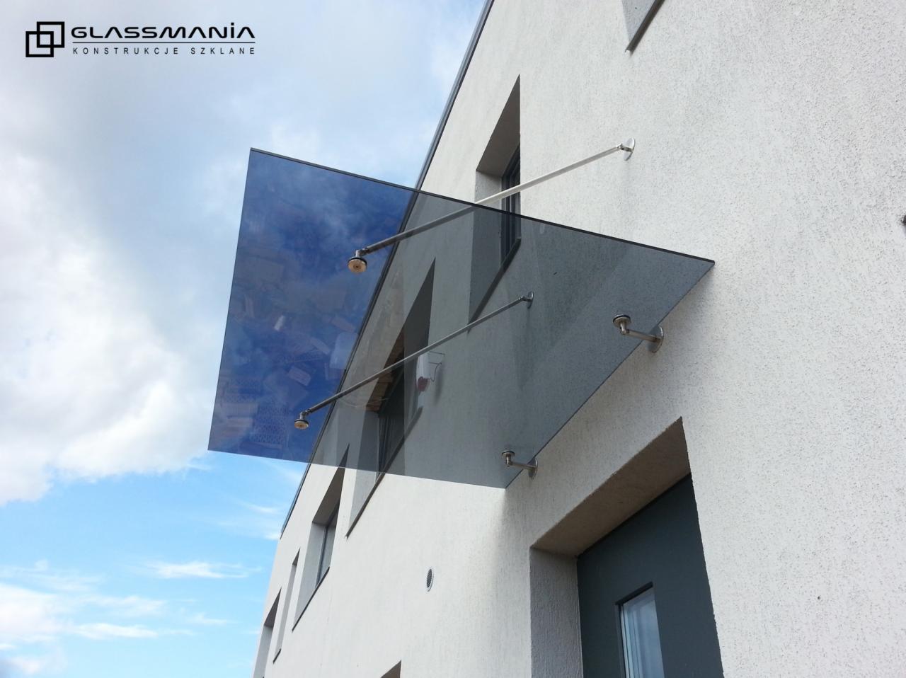 Szklany daszek nad wejściem do budynku z widocznym logotypem firmy Glassmania w górnym rogu zdjęcia.