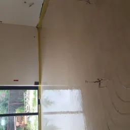 Świeżo wylana, mokra posadzka z widocznymi rurami ogrzewania podłogowego, zabezpieczona folią przy ścianie, z oknem w tle.