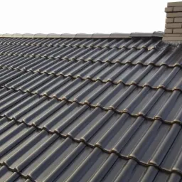 Błyszczący, ciemny dach z dachówki ceramicznej z kominem z cegły, widok z góry.