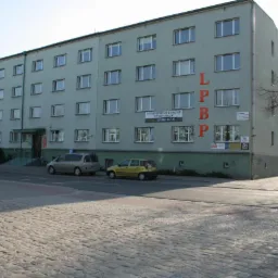 Budynek biurowy z napisem LPBP na elewacji, widok z ulicy z zaparkowanymi samochodami i chodnikiem wyłożonym kostką.