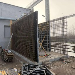 BOL-BUD Dariusz Bolek - Konstrukcja zbrojeniowa z siatki stalowej i szalunków na budowie, widok z boku, z narzędziami i materiałami budowlanymi w tle, pochmurny dzień.