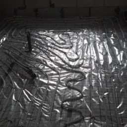 Montaż rur ogrzewania podłogowego na folii izolacyjnej z siatką, widoczne surowe ściany z bloczków.