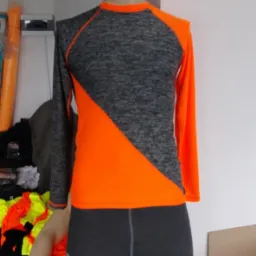 Manekin prezentuje komplet odzieży sportowej: szarą koszulkę z długim rękawem z pomarańczowymi wstawkami i szare legginsy.