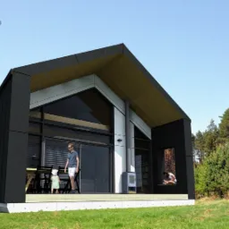 Wizualizacja nowoczesnego, czarno-białego domu z dużymi przeszkleniami, z osobami na tarasie i dronem w tle.