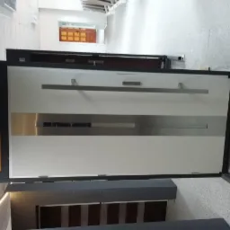 Ekspozycja stalowych drzwi zewnętrznych w salonie, widoczne logo 'seHo' na czarnym panelu bocznym, z długimi, poziomymi uchwytami i szarym, dekoracyjnym pasem na białej powierzchni drzwi.