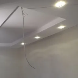 Sufit podwieszany z oświetleniem punktowym, widoczne wystające kable instalacji elektrycznej i surowe ściany w trakcie prac wykończeniowych.