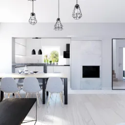 Jasne wnętrze z minimalistycznym kominkiem, stołem z szarymi krzesłami i widokiem na kuchnię w tle.