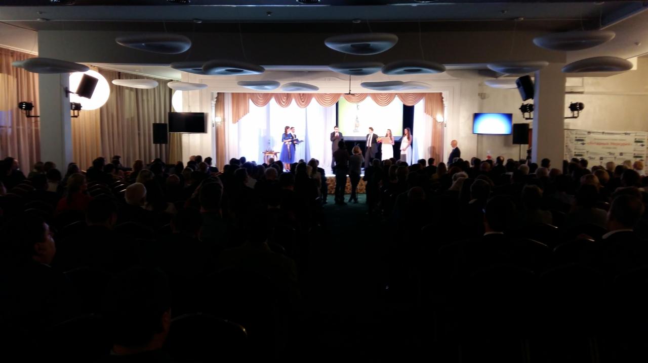 Sala konferencyjna wypełniona publicznością podczas uroczystości na scenie z oświetleniem punktowym i dekoracyjnymi lampami sufitowymi.