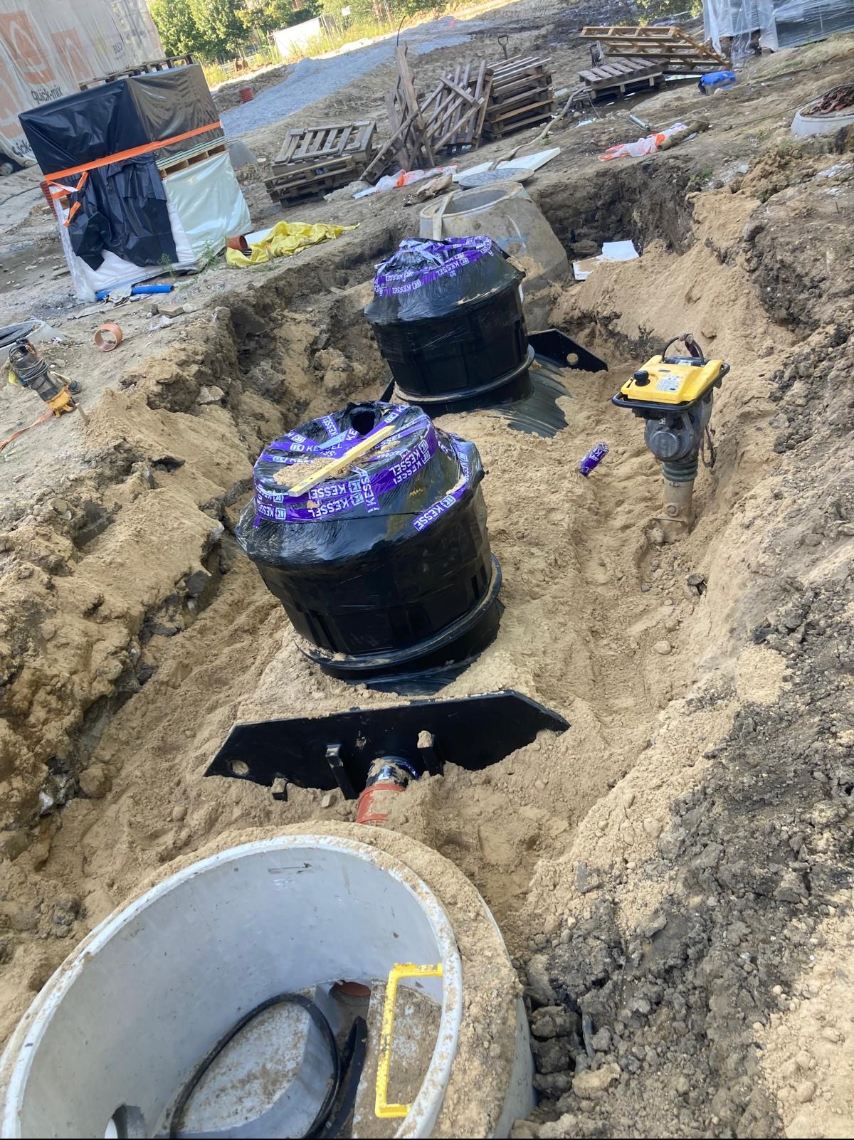 Montaż separatorów w wykopie, zabezpieczonych folią Kessel, na budowie we Wrocławiu. Widoczny ubijak wibracyjny i betonowy krąg. Prace ziemne.