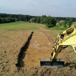 Żółta koparka w trakcie wykopu pod fundamenty w Stalowej Woli, widoczne ślady świeżej ziemi i wyznaczony obszar pod budowę.