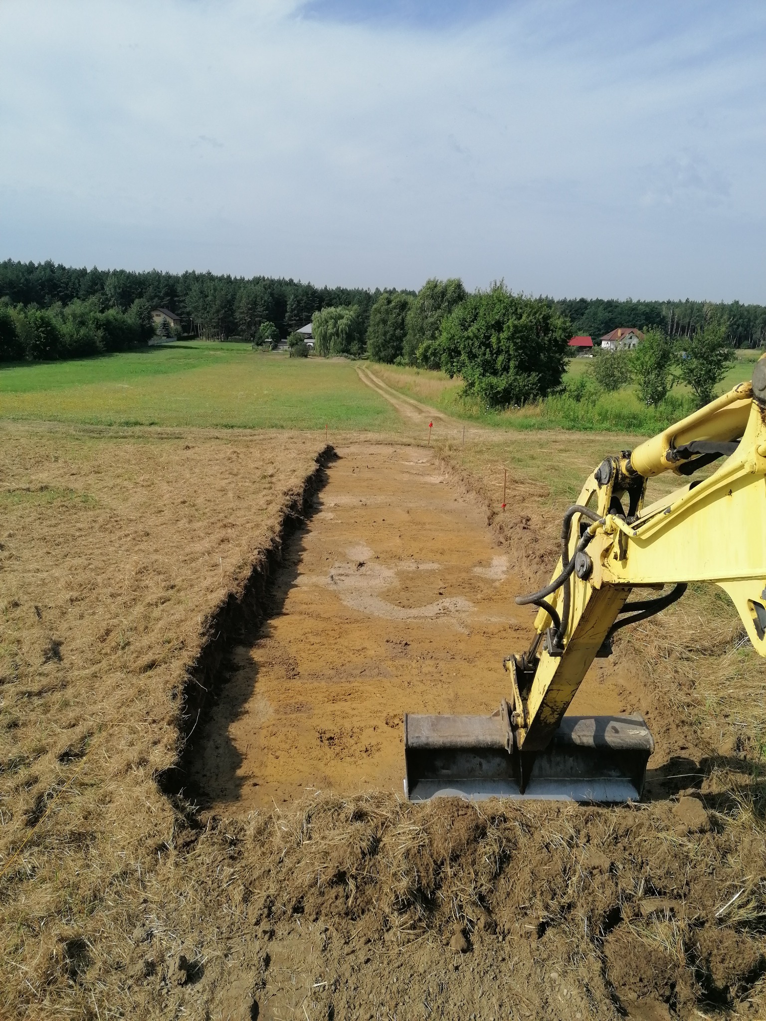Żółta koparka w trakcie wykopu pod fundamenty w Stalowej Woli, widoczne ślady świeżej ziemi i wyznaczony obszar pod budowę.