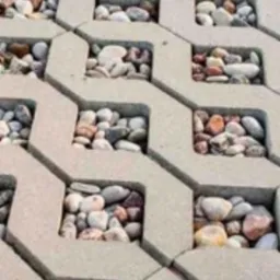 Szara, betonowa ażurowa nawierzchnia wypełniona dekoracyjnymi, drobnymi kamieniami o różnych odcieniach bieli, beżu i brązu.