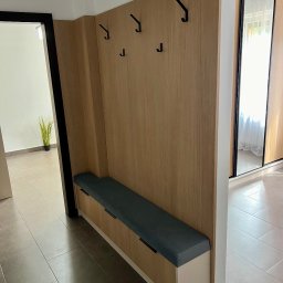 Meble Partyka Szymon Partyka - Wnęka z siedziskiem i wieszakami w przedpokoju, drewniane panele, obok szafa przesuwna z lustrem.