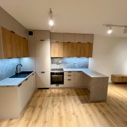 Meble Partyka Szymon Partyka - Nowoczesna kuchnia z drewnianymi i beżowymi frontami, szarym blatem i podświetleniem LED, na podłodze panele imitujące drewno.